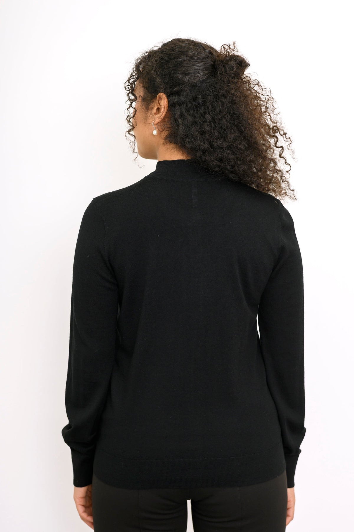 Back view of a woman wearing a black merino wool cardigan sweater showing ribbed hem construction.