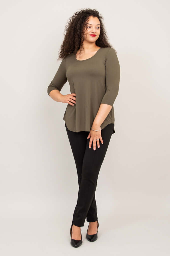 Woman standing in olive 3/4 sleeve top with hand on hip and black pants
