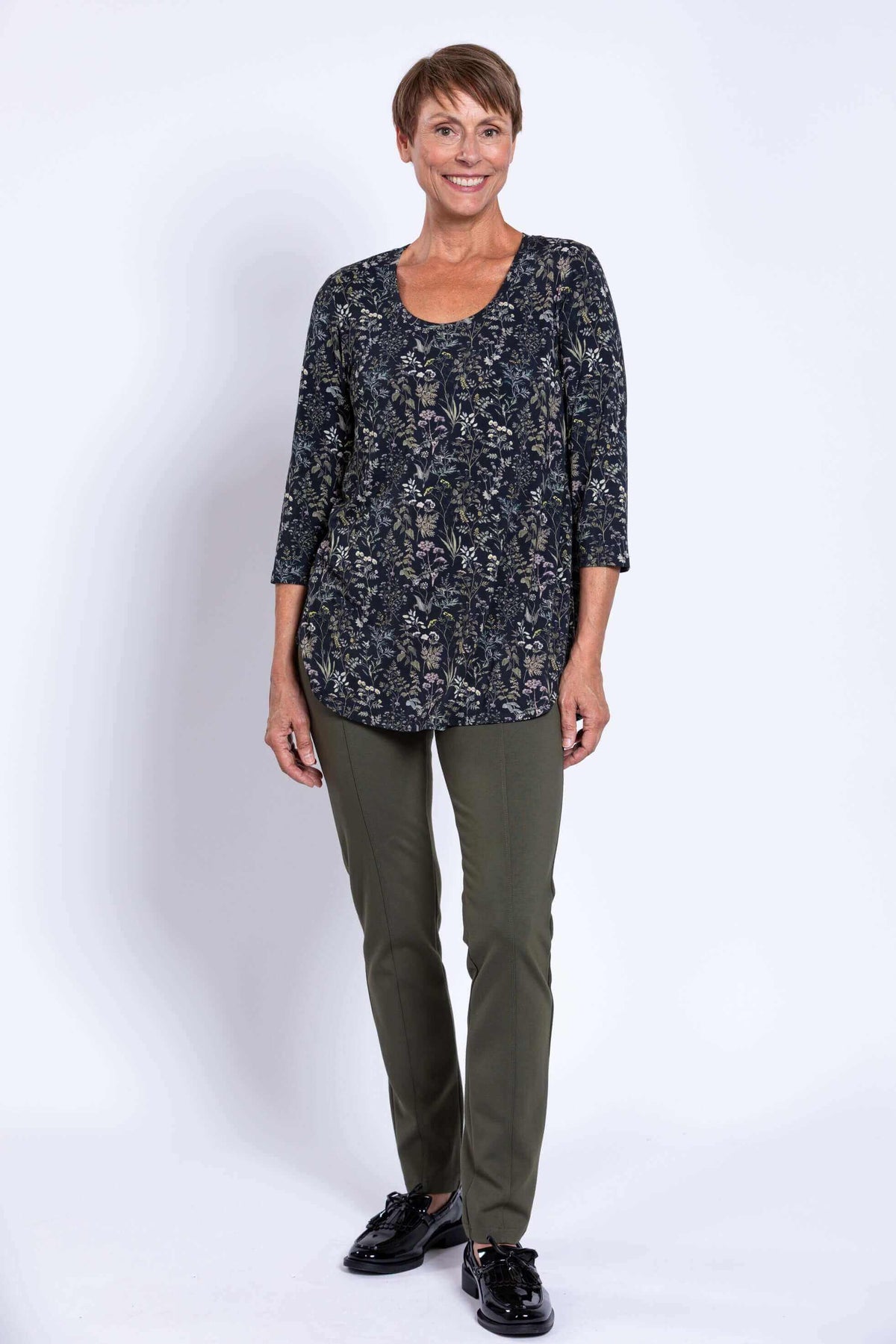 Woman standing and smiling in a black floral bamboo top and green pants