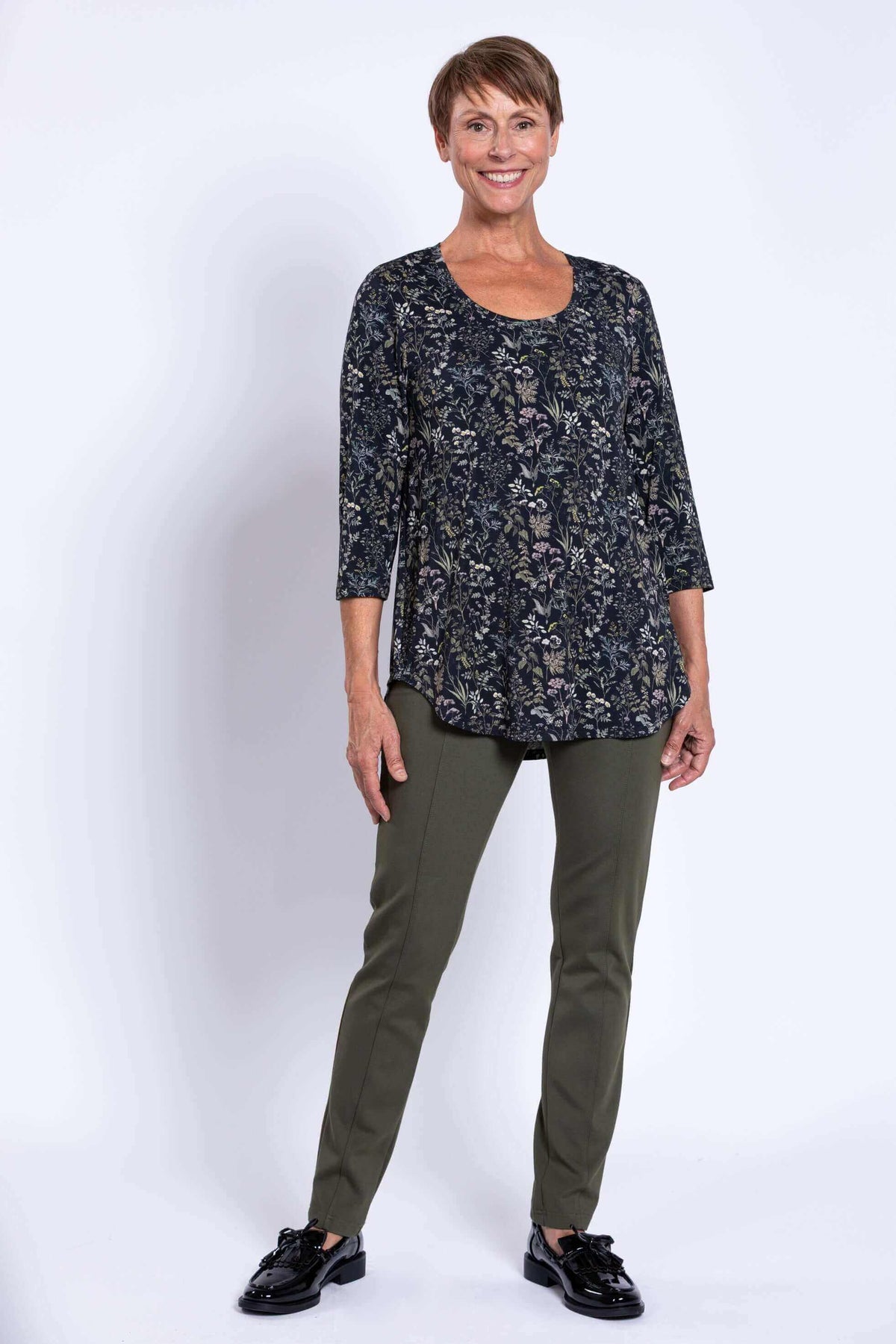 Full body view of a woman modeling a black floral 3/4 sleeve bamboo top with green pants