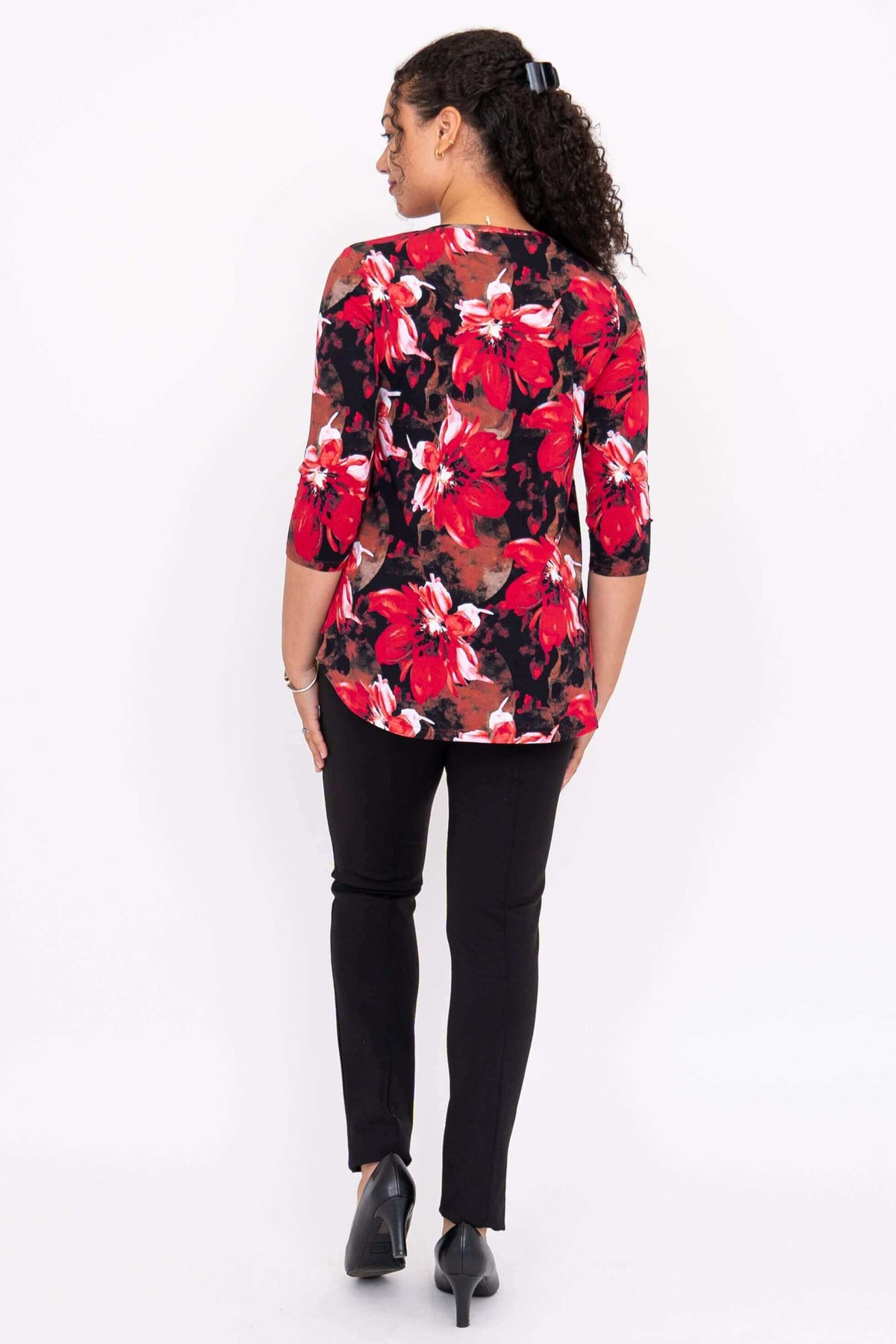 Back view of a woman wearing a red and black floral 3/4 sleeve top and black pants