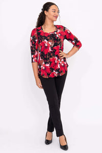 Woman in a red floral 3/4 sleeve top and black pants, standing with one hand on hip
