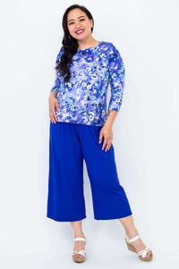 Smiling woman in a blue floral 3/4 sleeve tee and wide-leg pants with white sandals