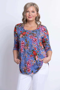 Close-up of woman in blue floral top with hands in pockets, smiling