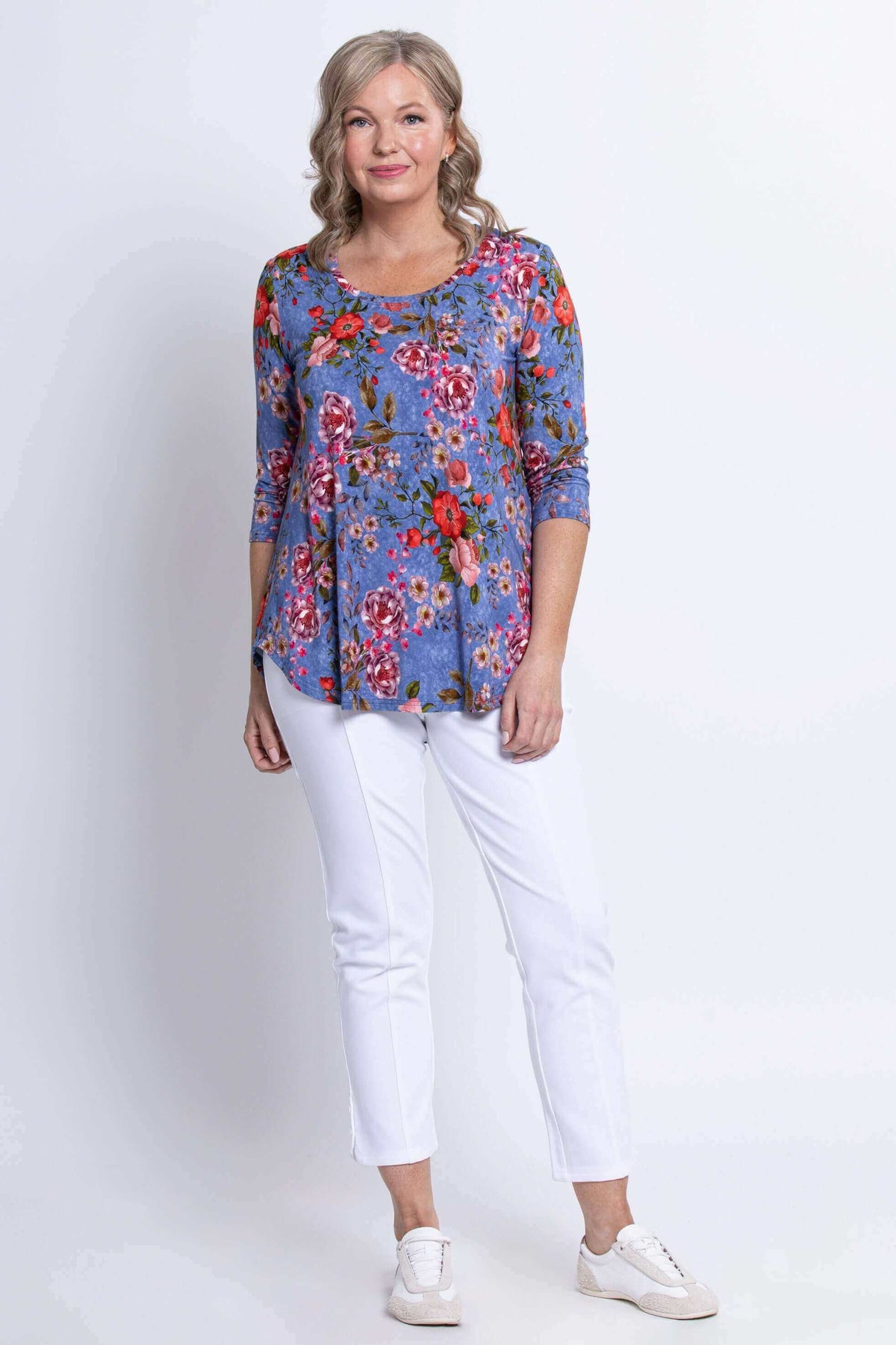 Full-length view of a woman in a blue floral top with white pants and sneakers