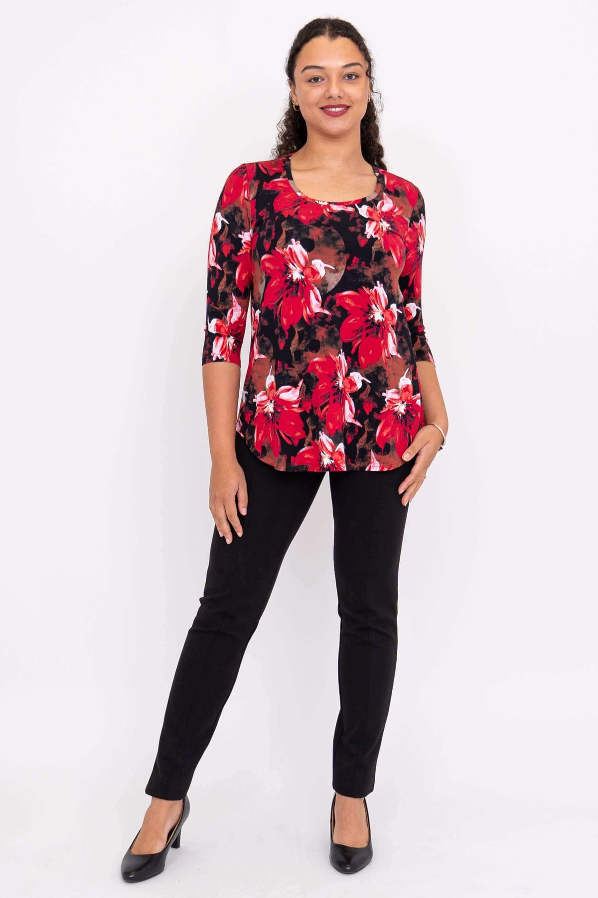 Woman standing in red floral print 3/4 sleeve top, black pants, and black heels