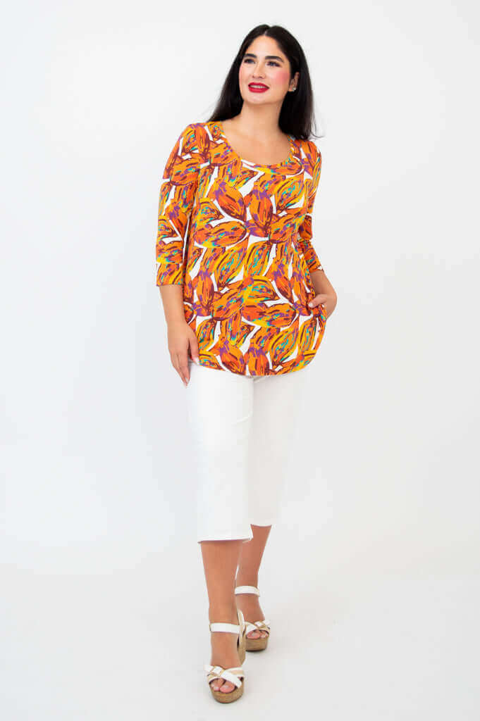 Woman modeling Jazz 3/4 sleeve tangerine splash top with white capris, angled front view
