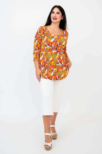Woman modeling Jazz 3/4 sleeve tangerine splash top with white capris, angled front view