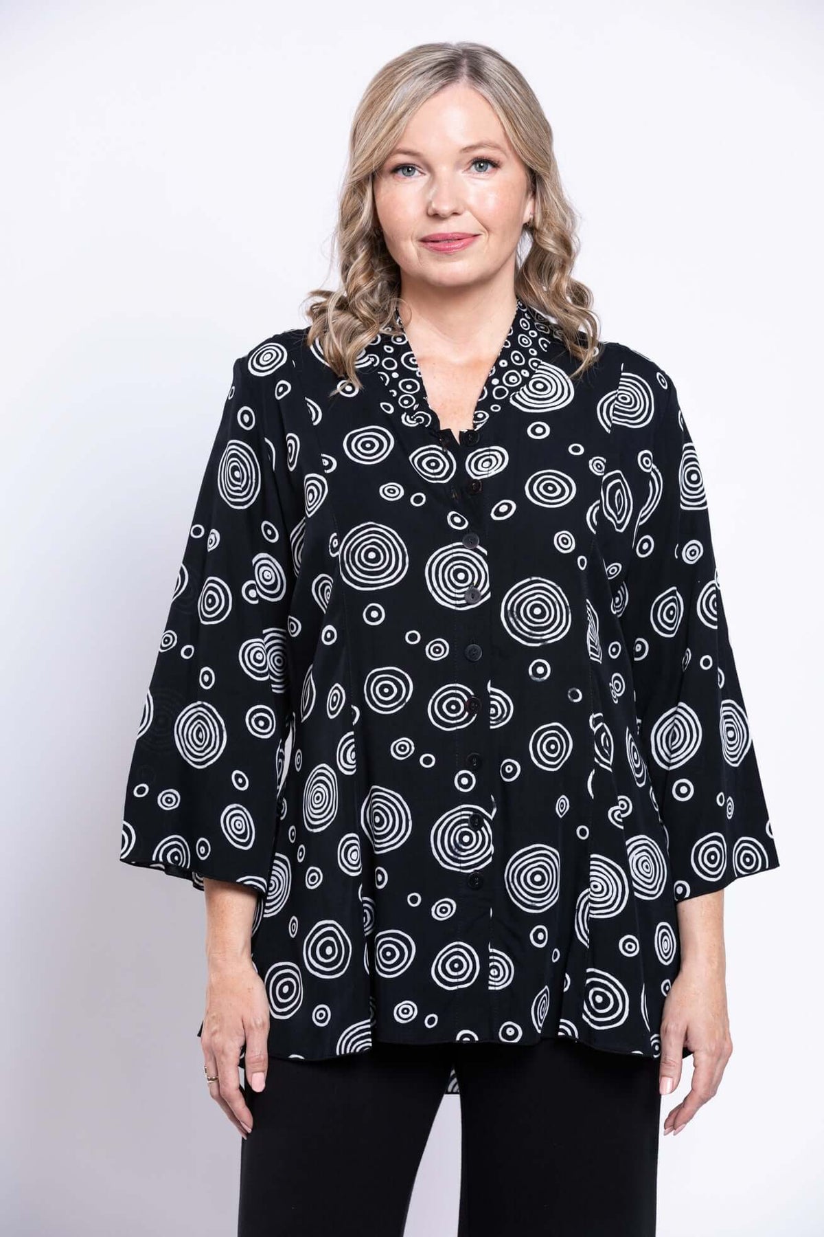 Front view of a woman wearing a black blouse with white circle pattern and 3/4 bell sleeves