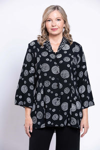 Front view of a woman wearing a black blouse with white circle pattern and 3/4 bell sleeves