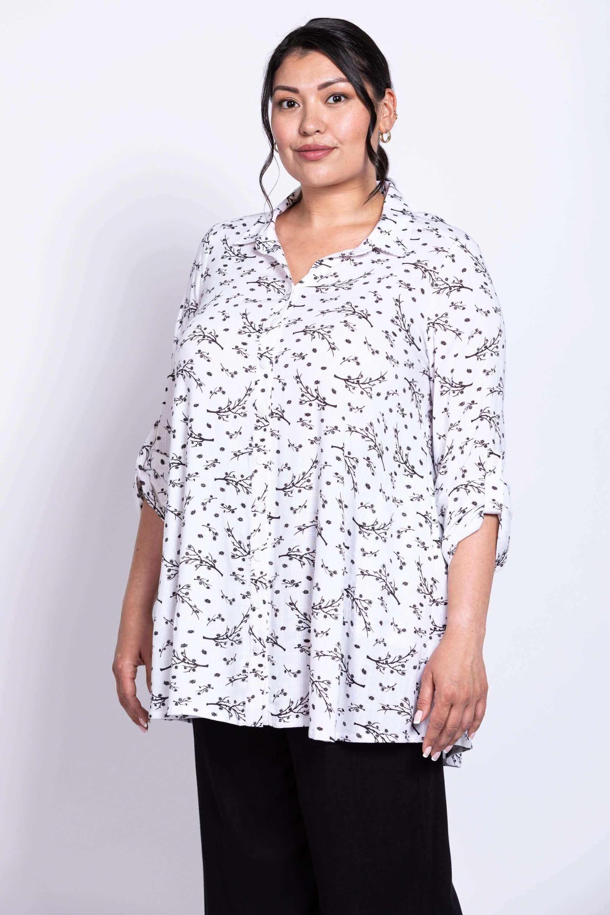 Front view of model wearing white bamboo linen tunic with petal print, 3/4 cuffs, and black pants