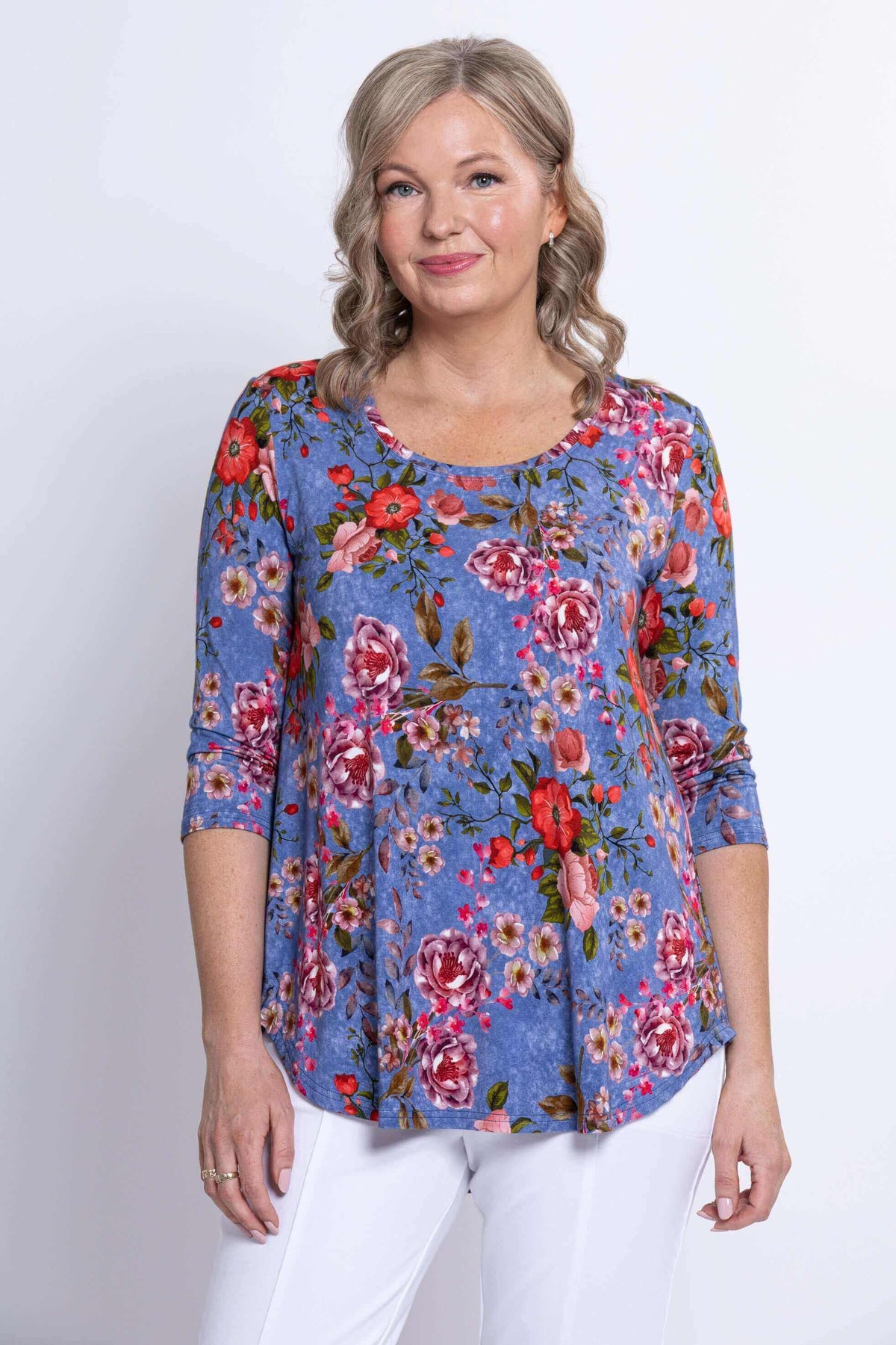 Model wearing a blue floral 3/4 sleeve top with pink and red flowers, front view