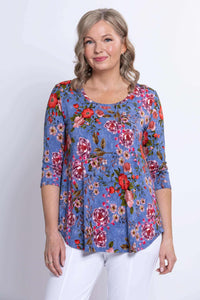 Model wearing a blue floral 3/4 sleeve top with pink and red flowers, front view