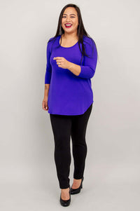 Woman in a purple 3/4 sleeve bamboo top and black pants, walking and smiling.