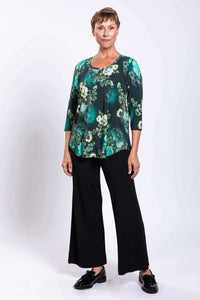 Three-quarter front view of woman in green floral 3/4 sleeve bamboo top and black pants