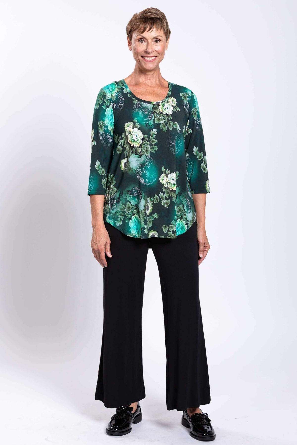 Full front view of woman wearing green floral 3/4 sleeve bamboo top with black pants
