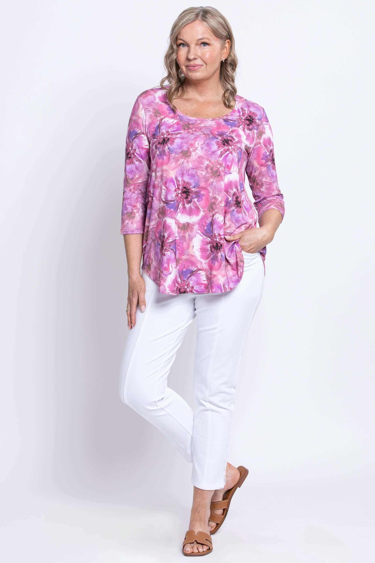 Full body view of woman posing in pink and purple floral 3/4 sleeve bamboo top and white pants