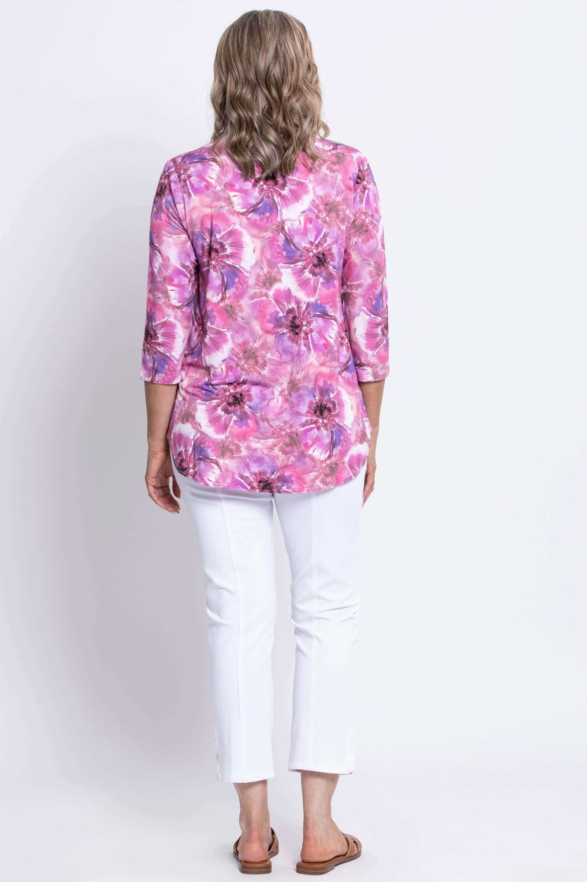 Back view of woman wearing pink floral top with rounded hem styled with slim fit white pants