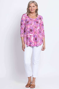 Woman modeling with her arms relaxed in a pink floral top, white pants, and tan colored sandals