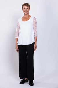 Angled front view of a woman in a white lace overlay top with 3/4 sleeves and black pants