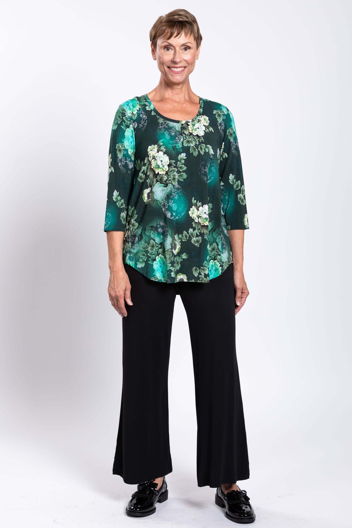 Woman standing in a green floral bamboo 3/4 sleeve top with black wide-leg pants
