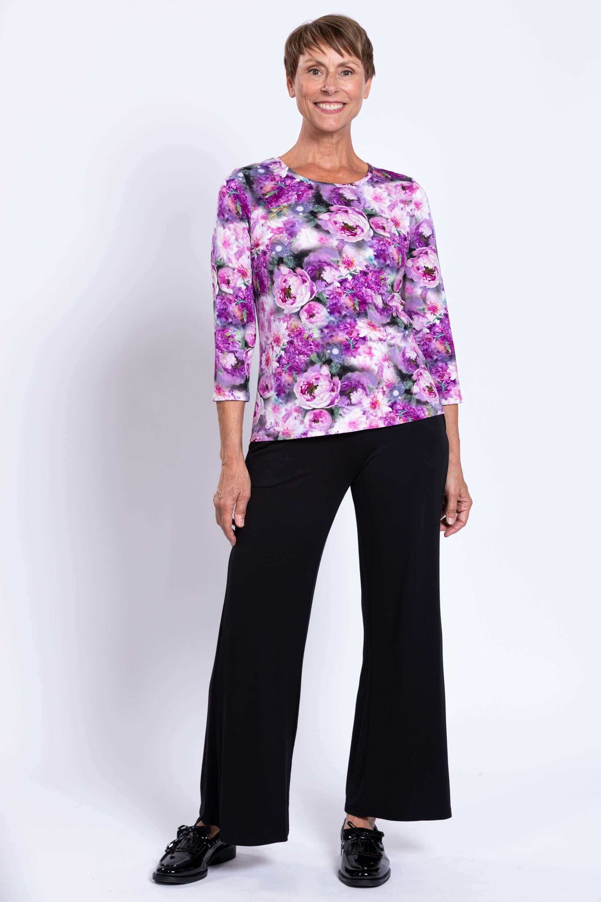 Woman smiling in a purple floral 3/4 sleeve top and black trousers