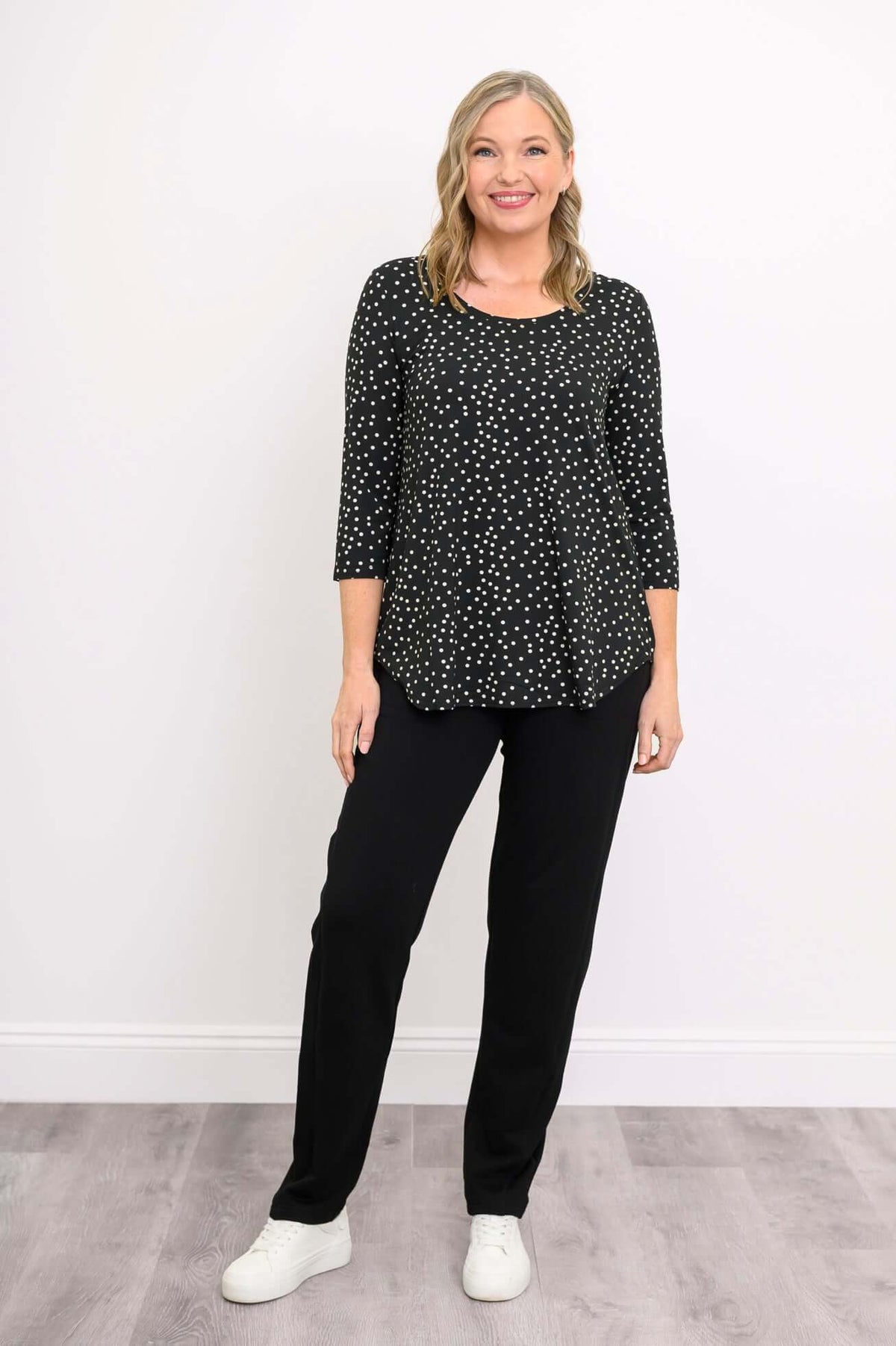 Blonde woman smiling in black polka dot bamboo 3/4 sleeve top and white sneakers