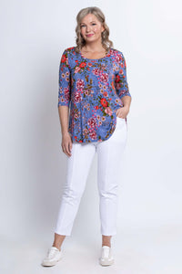 Woman standing with hand in pocket, wearing blue floral 3/4 sleeve bamboo top and white pants