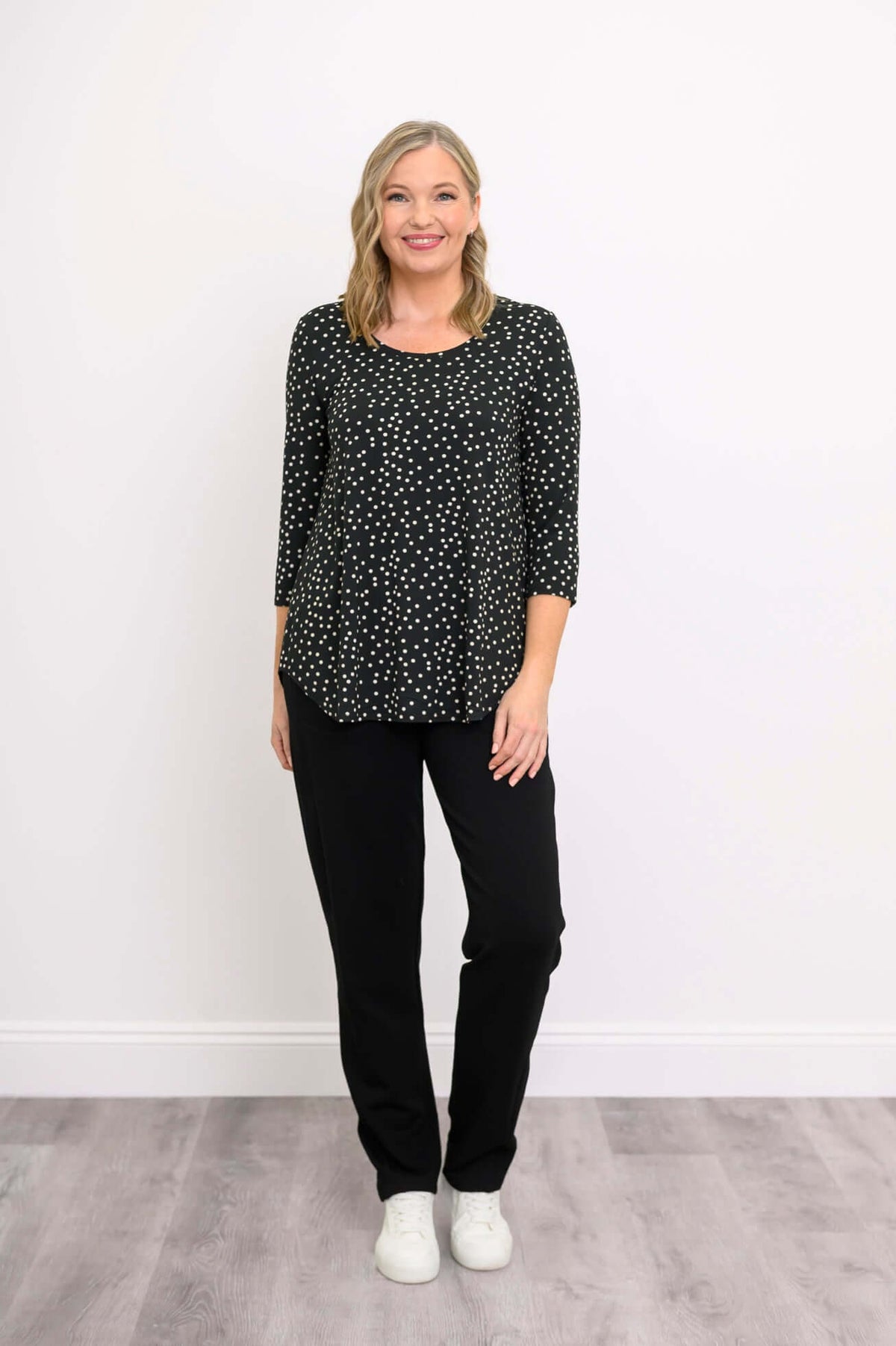 Blonde woman in polka dot bamboo 3/4 sleeve top with black pants, smiling