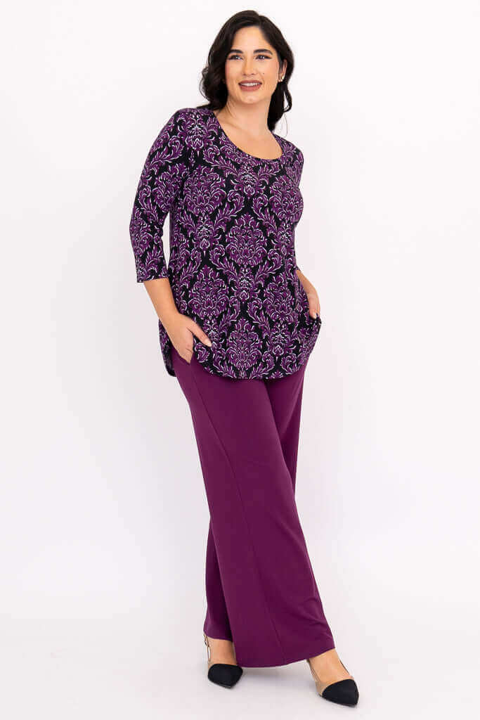Side view of woman in purple damask Jazz 3/4 sleeve top and purple pants, hand in pocket