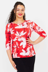 Woman wearing a red and white floral 3/4 sleeve top with wide neckline and silver grommet detail