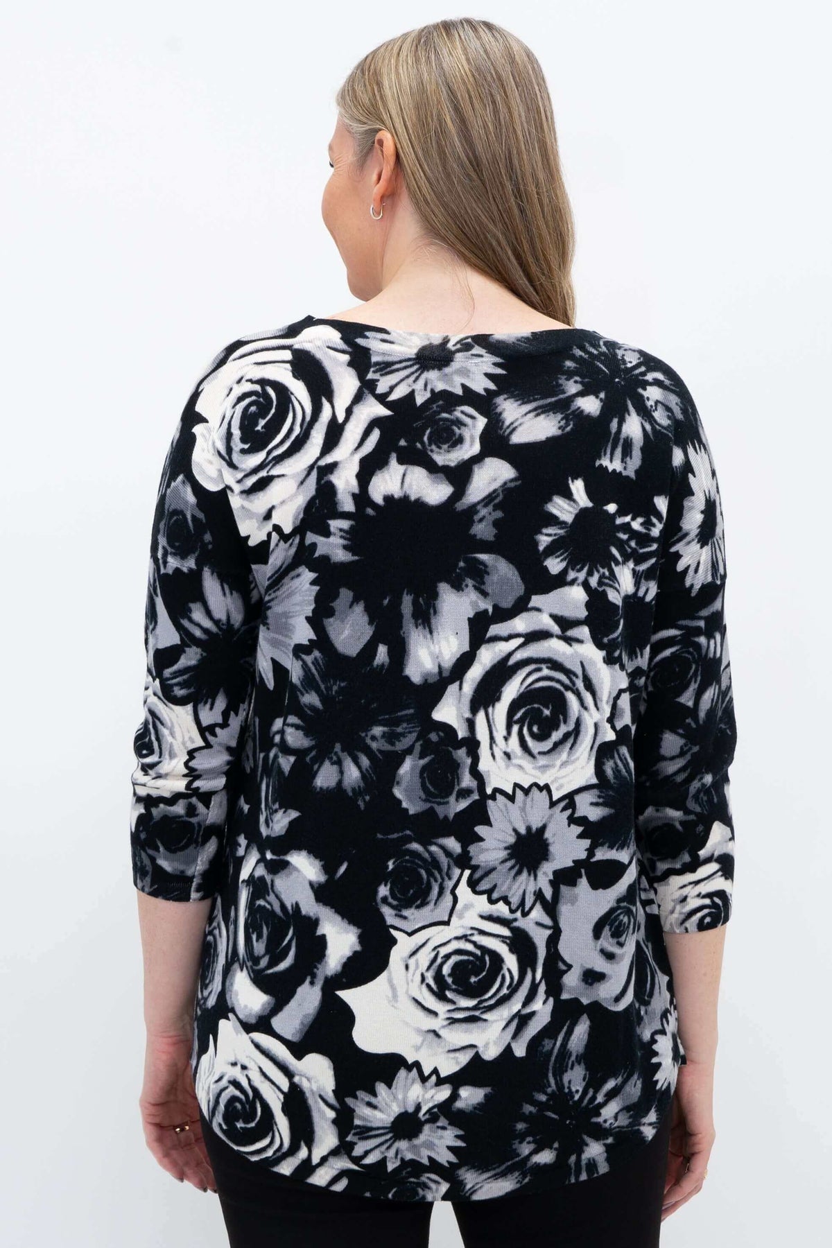 Back view of a woman in a black and white floral pullover sweater showing rounded hem