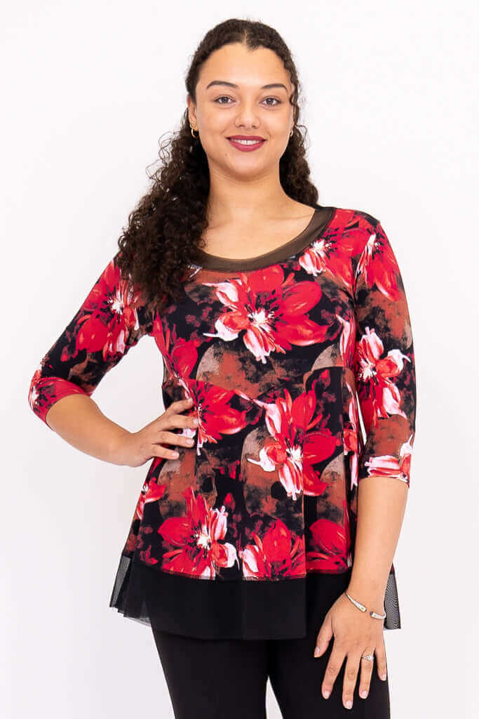 Woman wearing a vibrant red floral top with mesh neckline and 3/4 sleeves, hand on hip