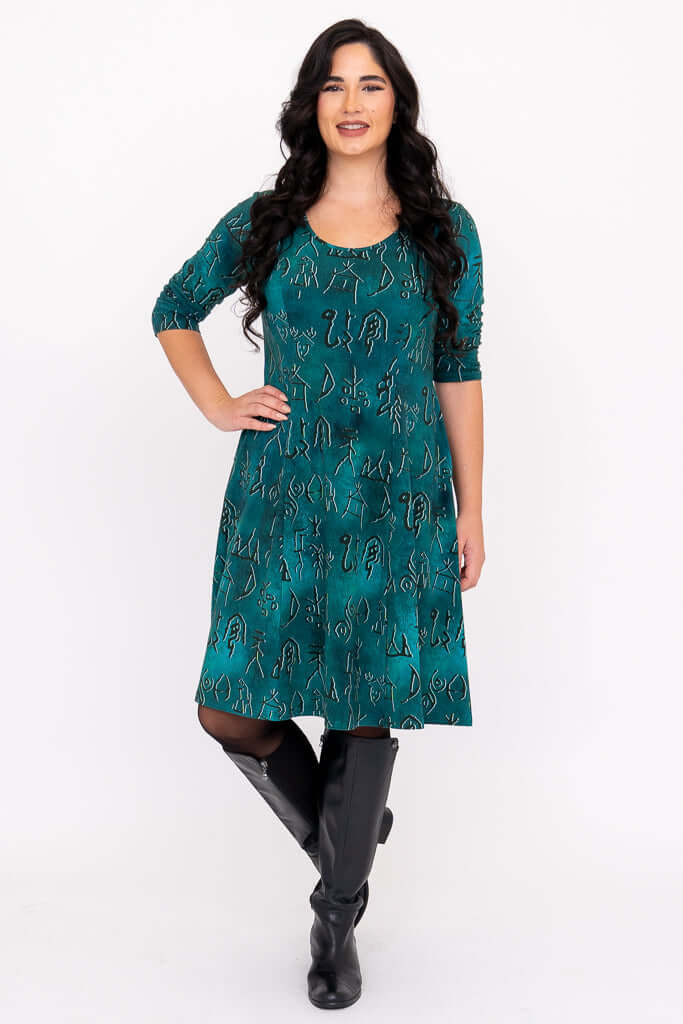 Model posing in teal Callie dress with hand on hip, showcasing side pockets and printed symbols