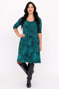 Model posing in teal Callie dress with hand on hip, showcasing side pockets and printed symbols