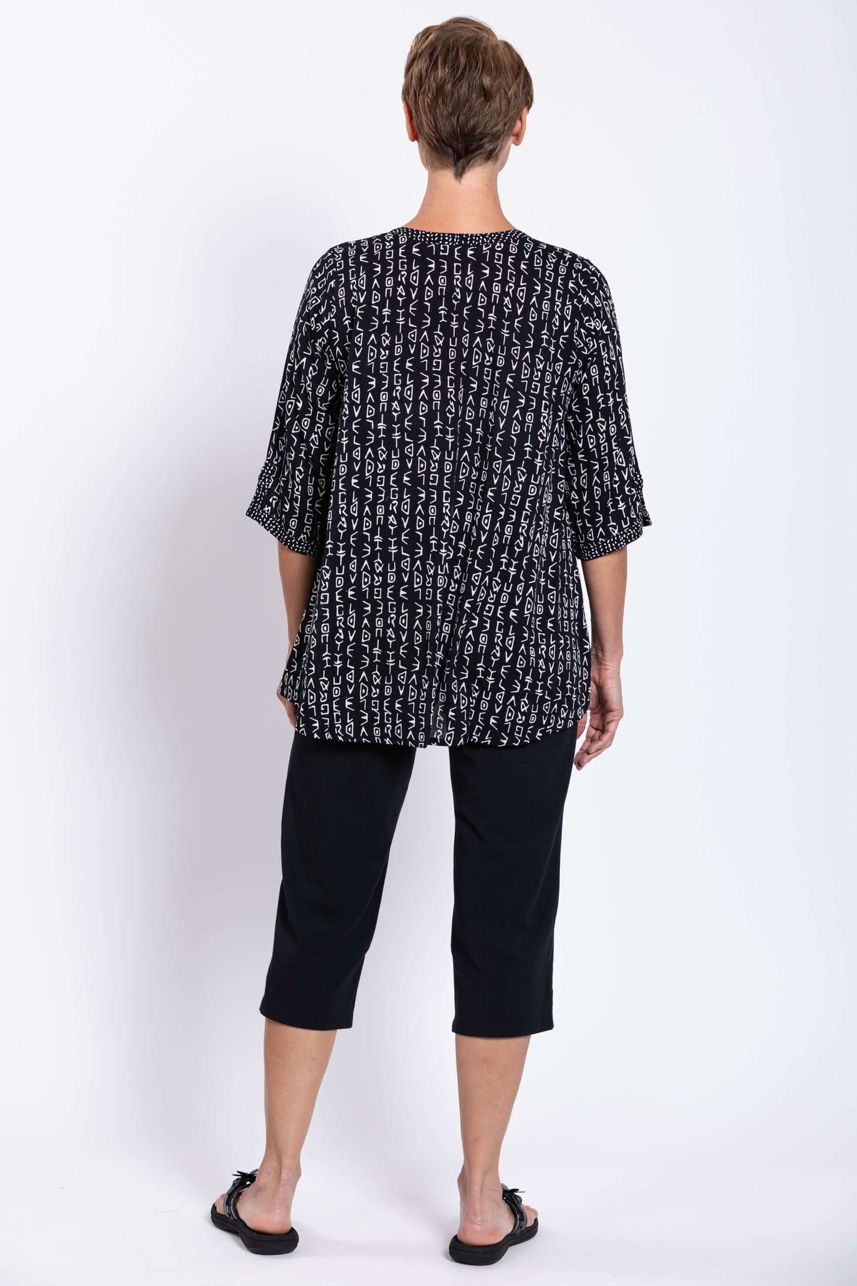 Back view of a woman wearing a black and white abstract print blouse with 3/4 sleeves