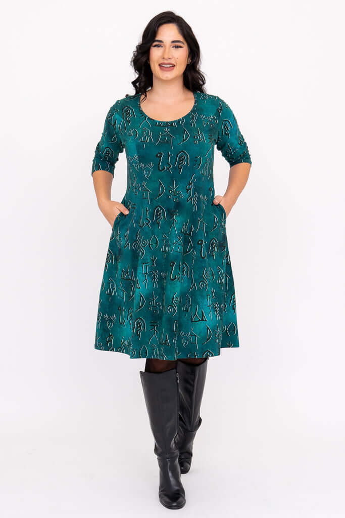 Model smiling in teal Callie dress, hands in pockets, with 3/4 sleeves and unique symbol print