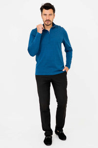 Man in blue 1/4 zip sweater, one hand by collar, other in pocket, black pants