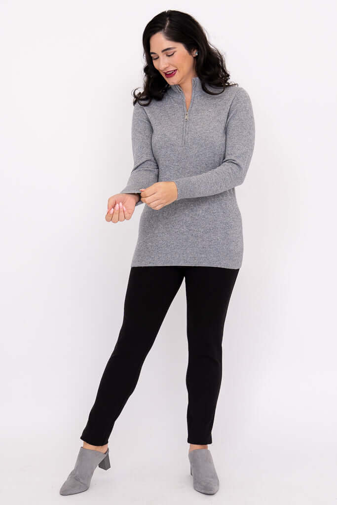 Woman adjusting sleeves of a grey half-zip sweater with black pants
