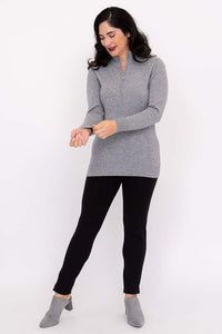 Woman adjusting sleeves of a grey half-zip sweater with black pants