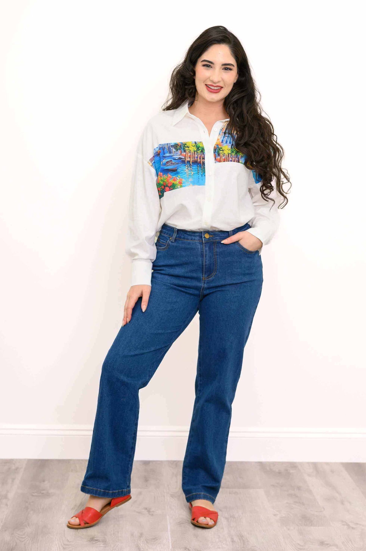 Model poses in Alex Blouse, white shirt with bright artistic design paired with denim jeans