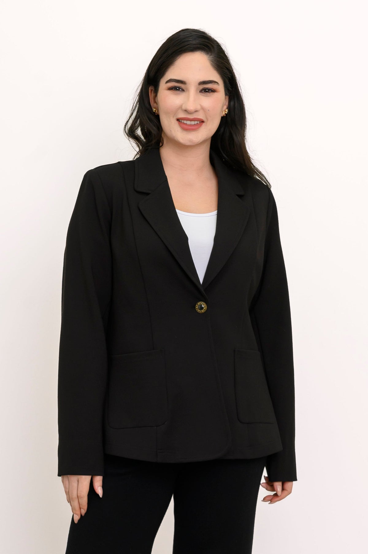 Woman wearing a black suit standing against a white wall.