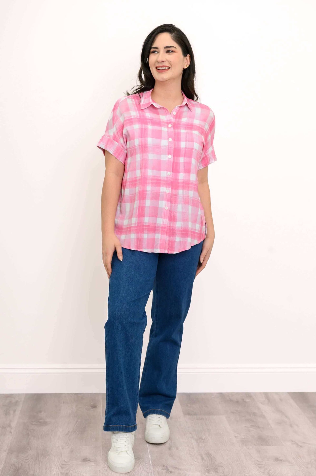 Angle view of a woman in a pink plaid blouse with rolled sleeves and blue jeans