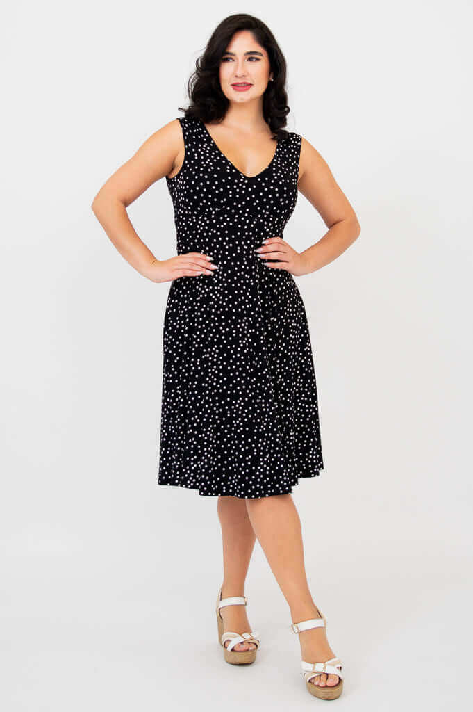 Angled front view of woman wearing sleeveless black polka dot dress and wedge sandals