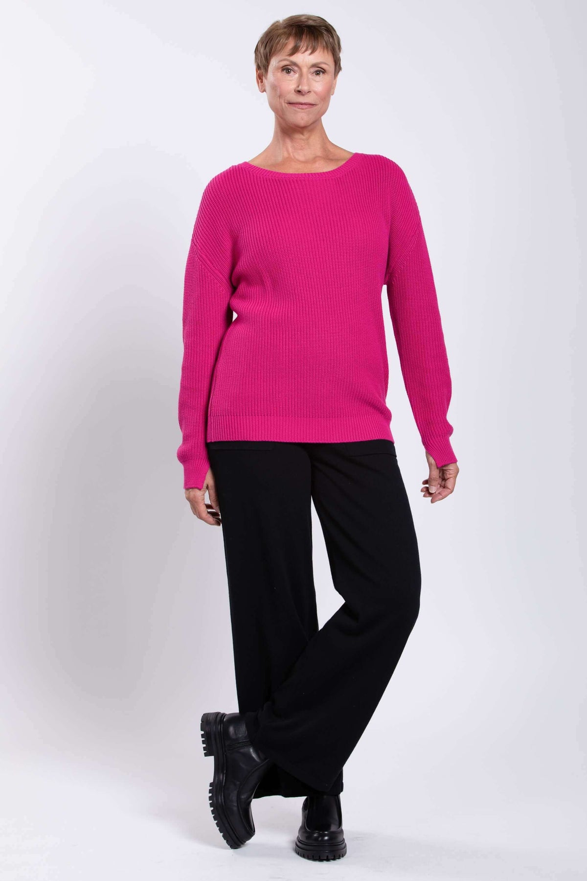 Angled front view of a woman in a fuchsia shaker stitch sweater and black pants