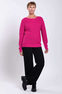 Angled front view of a woman in a fuchsia shaker stitch sweater and black pants