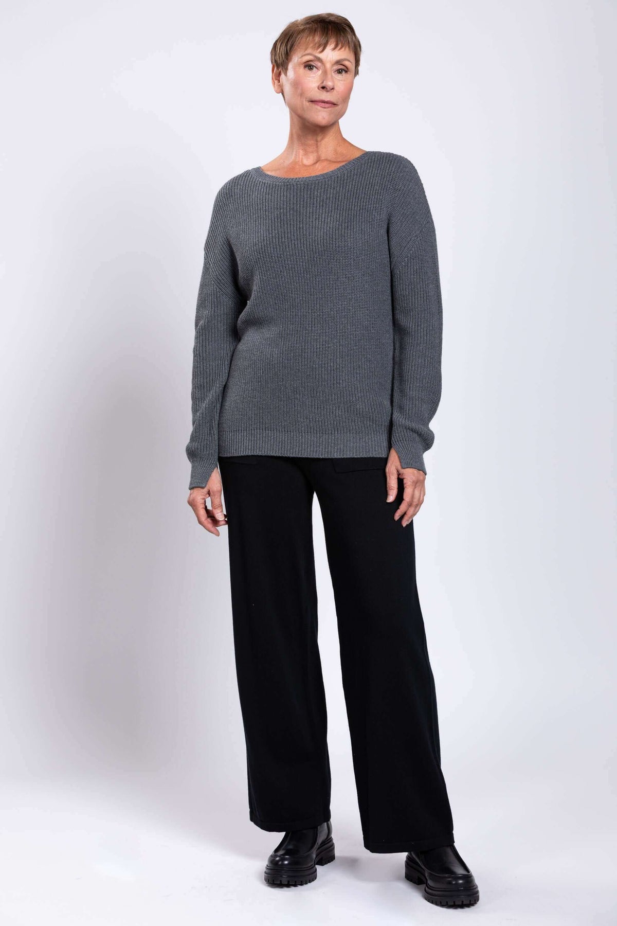 Angled front view of woman in grey knit sweater and black trousers
