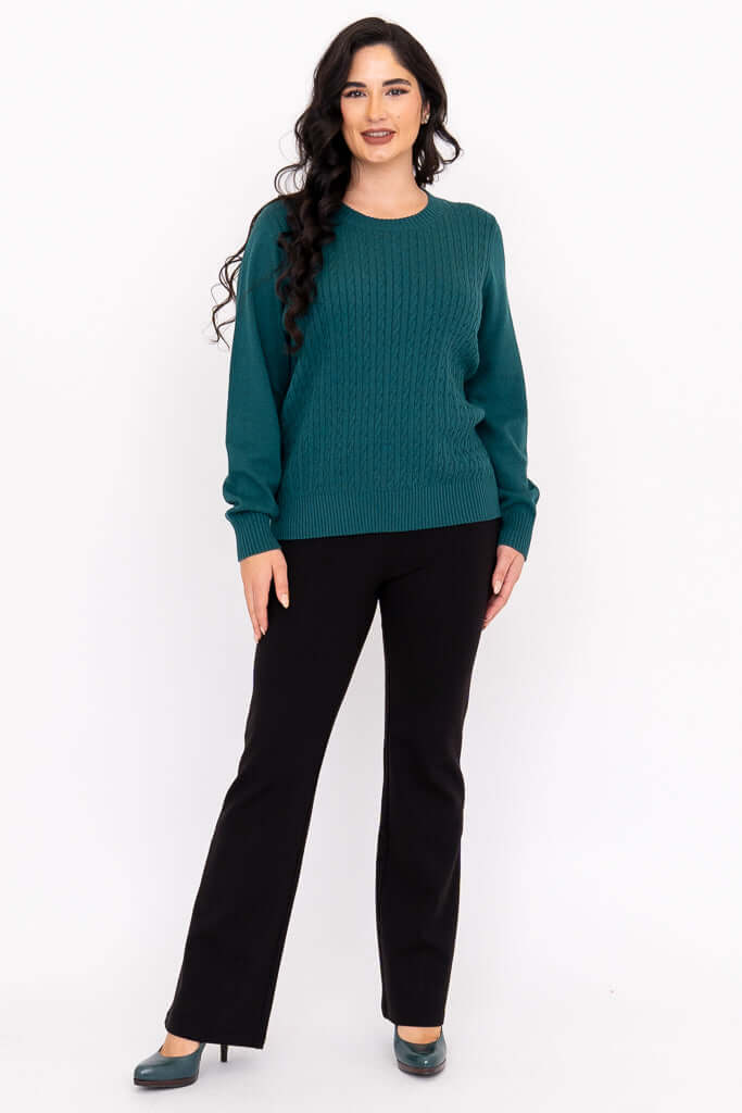 Woman in a teal cable knit sweater with black pants and teal shoes, angled front view