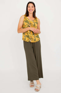 Woman posing in full outfit with yellow tropical tank top and olive green wide-leg pants, angled view