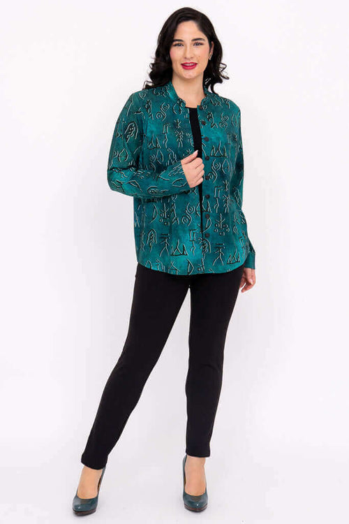 Woman posing in emerald patterned button-up top and black pants, angled view